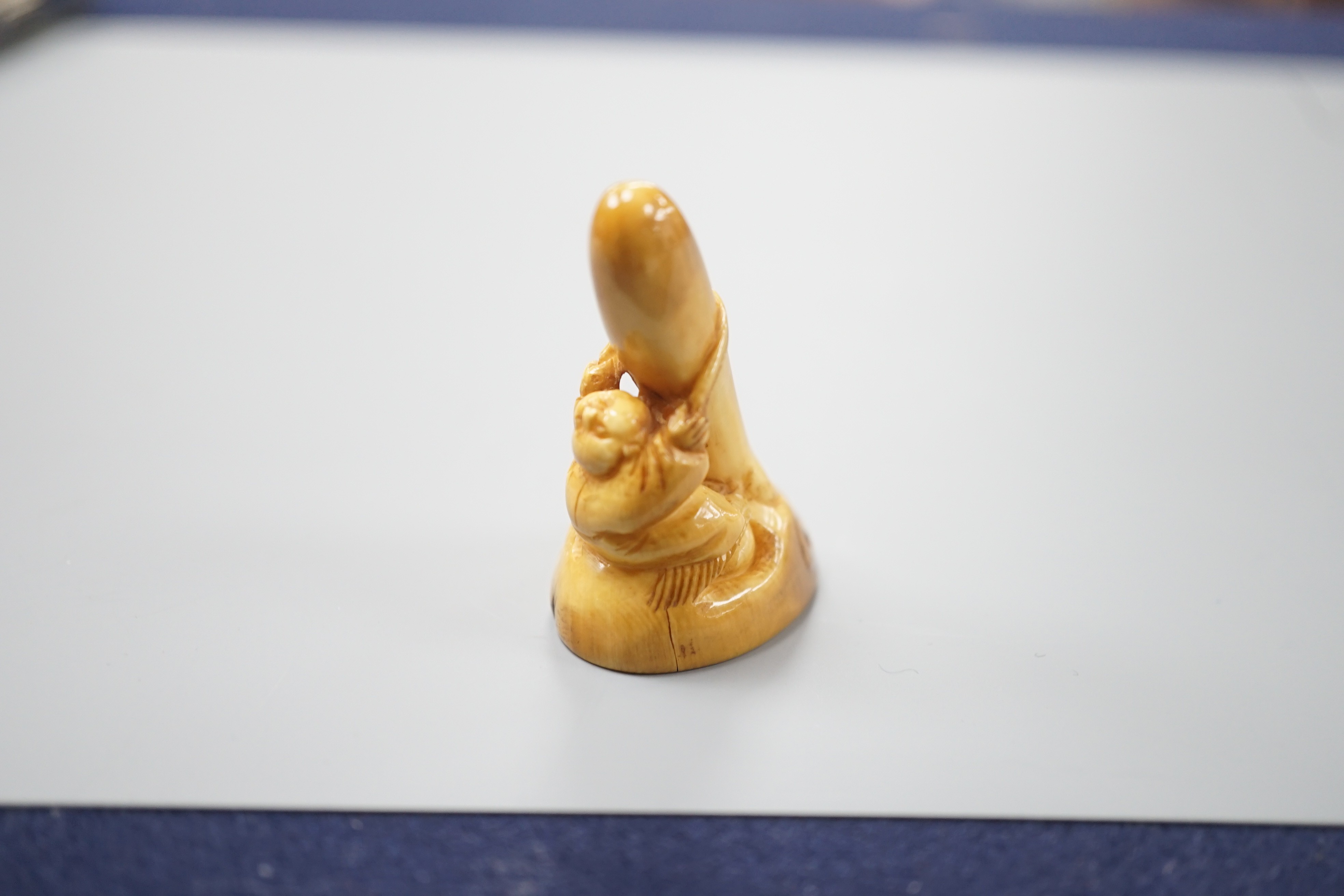 A Japanese ivory netsuke of a man climbing a giant Tengu noh mask, 19th century, 4.2cm
